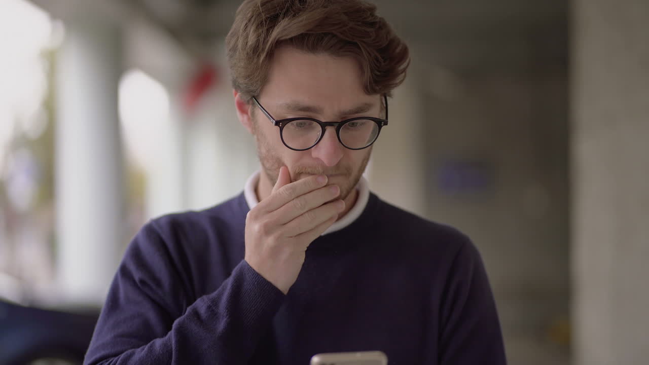 hombre nervioso con gafas usando un teléfono inteligente al aire libre