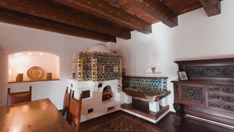 room with a large fireplace with tiled fasade and lots of wooden elements and furniture. interior of bran castle, romania.