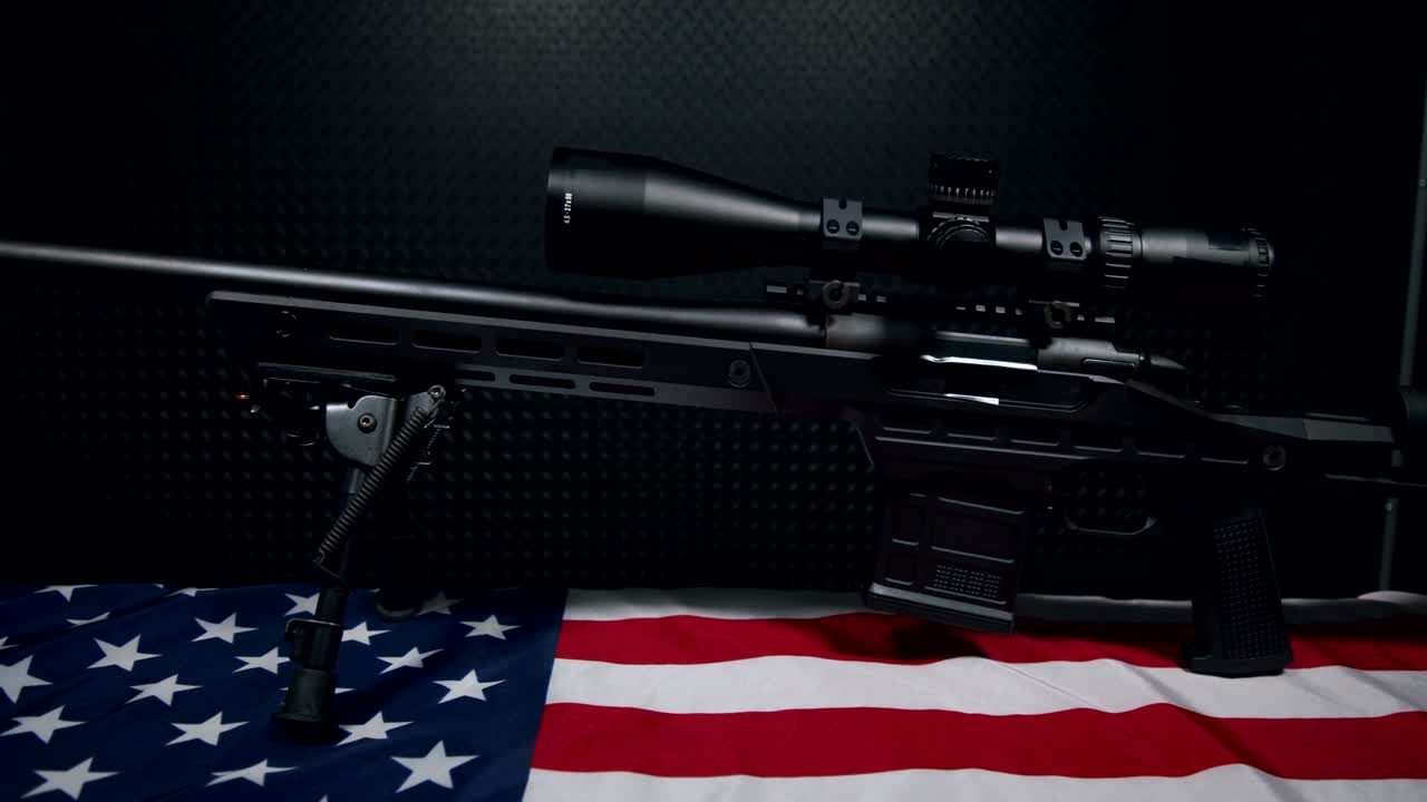 black Sniper Rifle with high powered Scope and ten round Magazine on American flag with dark background, left hand side view, slow pan left to right, 4k