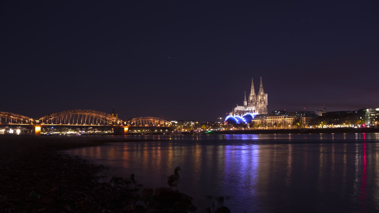 Colorful timelapse with Cologne Cathedral and Hohenzollernbridge in the background and rhine river with rocks in the foreground.Ships are passing and the Camera makes a nice, smooth move.