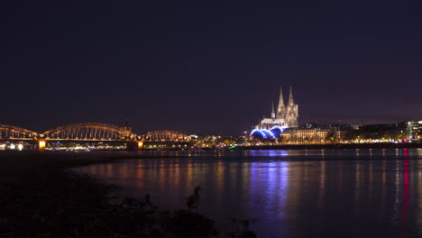 colorful timelapse with cologne cathedral and hohenzollernbridge in the background and rhine river with rocks in the foreground.ships are passing and the camera makes a nice, smooth move.