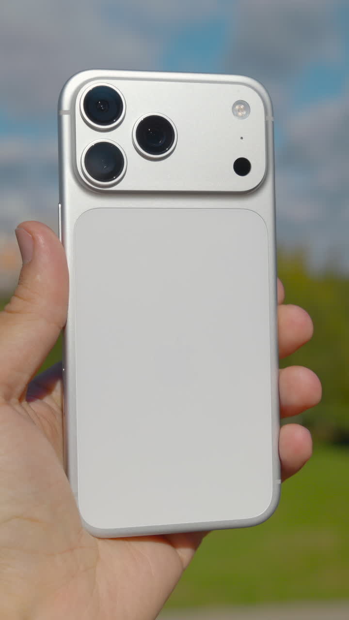 Male hand presenting a futuristic smartphone concept with a triple camera system outdoors. Action