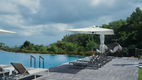 sunbeds with umbrellas on the poolside of resort villas during cloudy day in bali, indonesia. wide shot