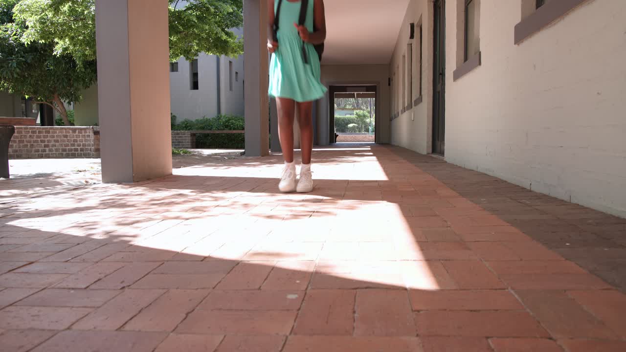Teenage woman in mint dress emerging, walking on walkway holding backpack straps, heading to class