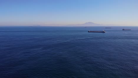 large bulk carrier sails from algeciras in the strait of gibraltar while passing another freighter en route to the atlantic with in the background the coast of africa and anchored ships
