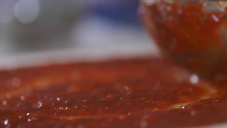 pizza tomato sauce being spread across dough using ladle