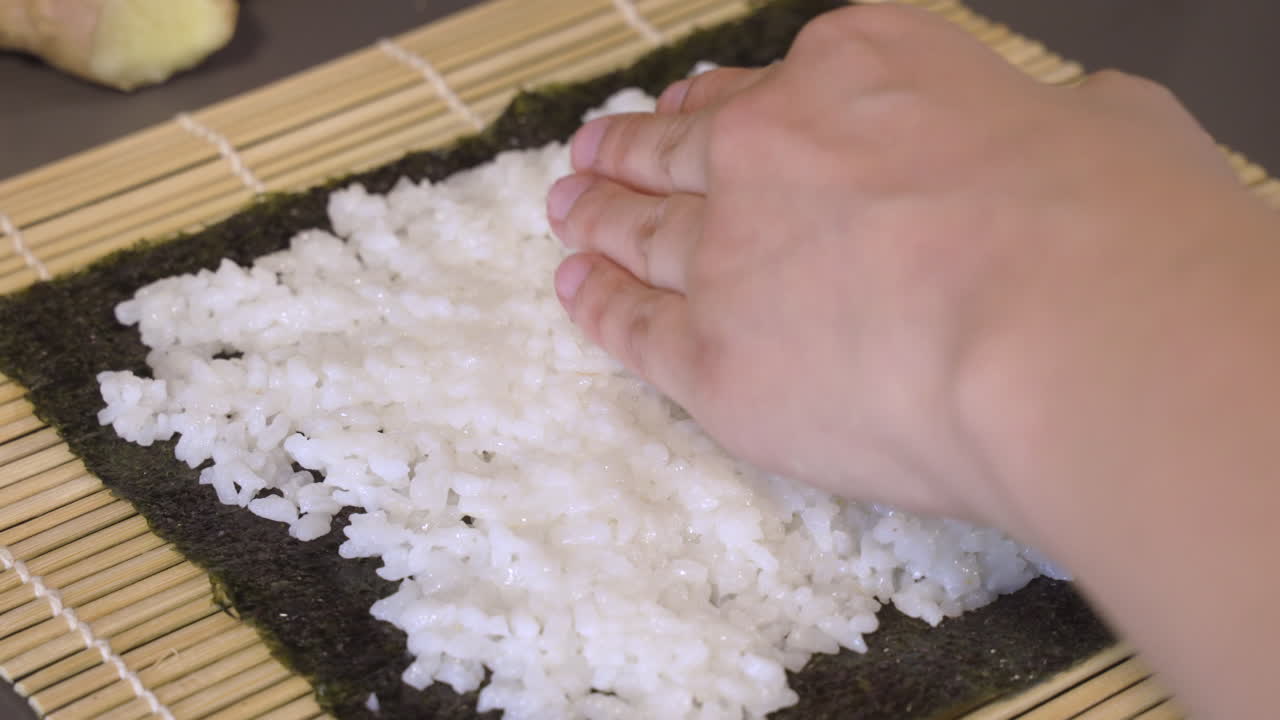 manos de un chef poniendo y presionando suavemente una fina capa de arroz blanco en la hoja de nori