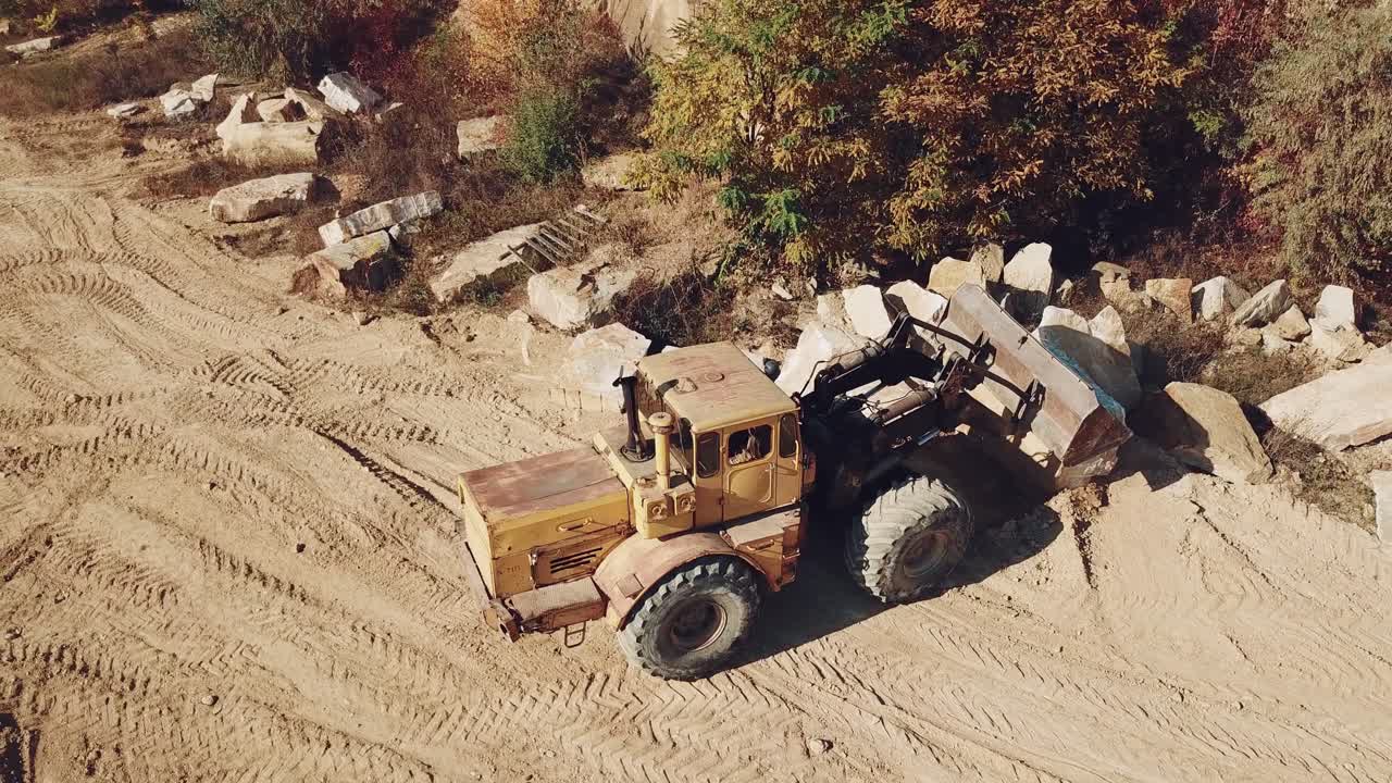 specially equipped machine with a bucket id working near a quarry with stones on the background of sand.