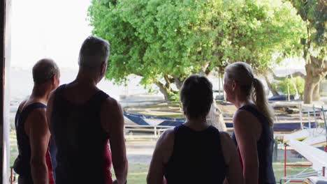 cuatro hombres y mujeres caucásicos mayores de pie junto a un río hablando