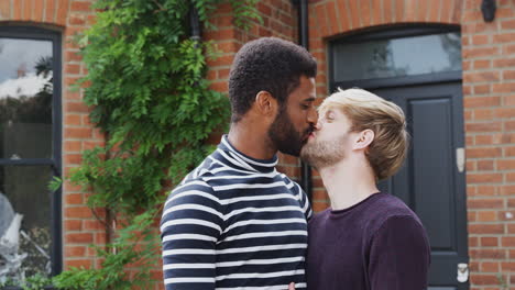 portrait of gay male couple standing outside new home on moving day together kissing