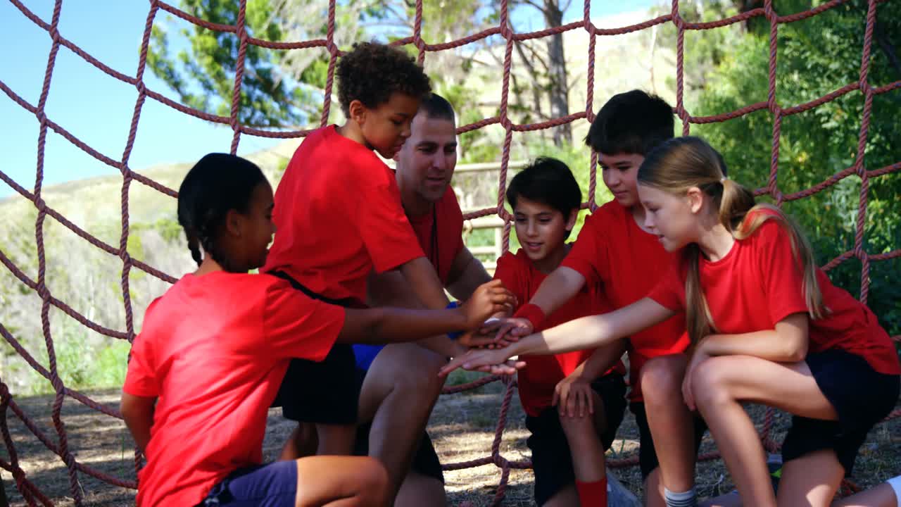 entrenador y niños formando una pila de manos en el campamento de entrenamiento