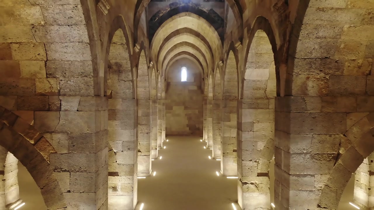 Vista interna di un'antica sala a volta in pietra con archi.