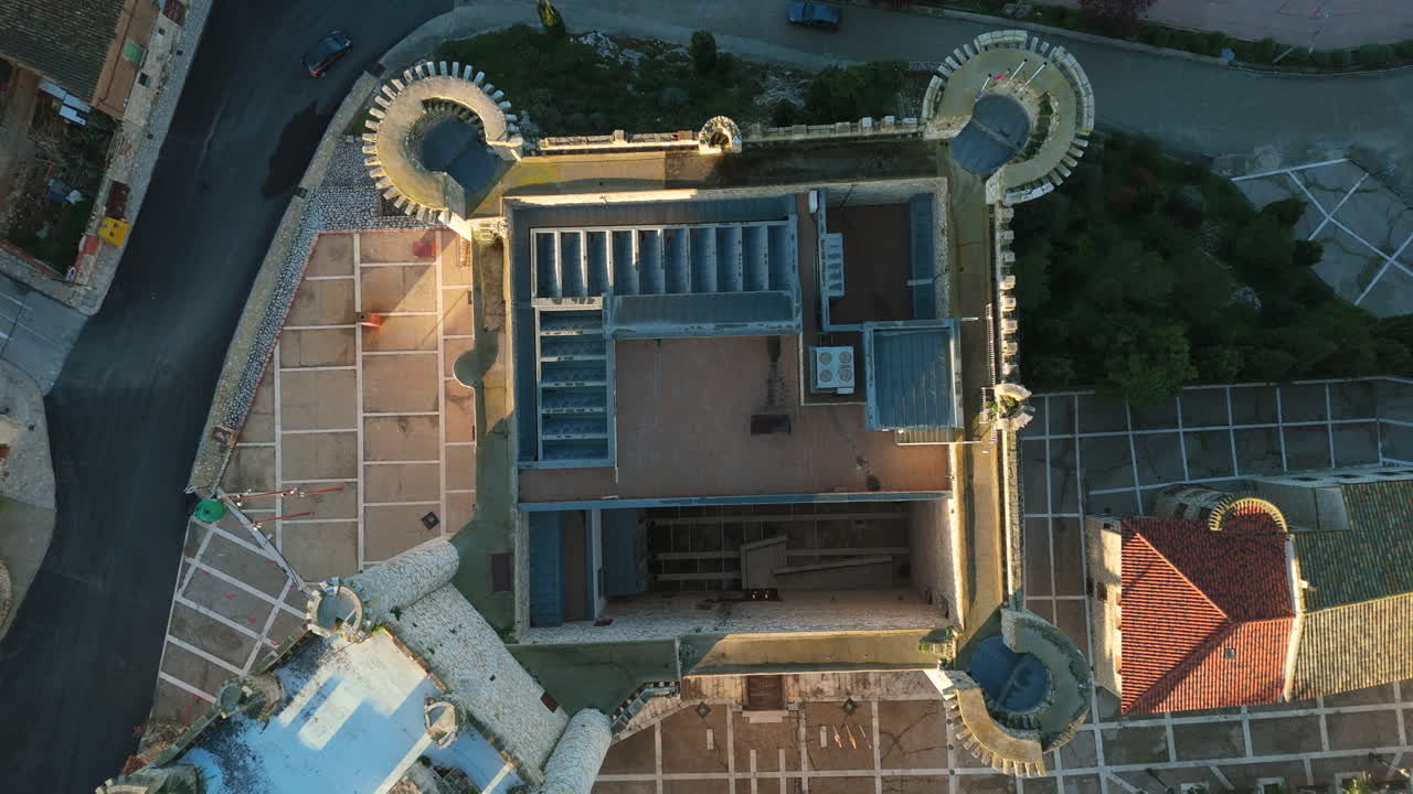 Cinematic top-down drone shot rising above a medieval castle in Torija, Guadalajara, Spain, revealing its symmetrical structure and surrounding urban layout in golden hour light