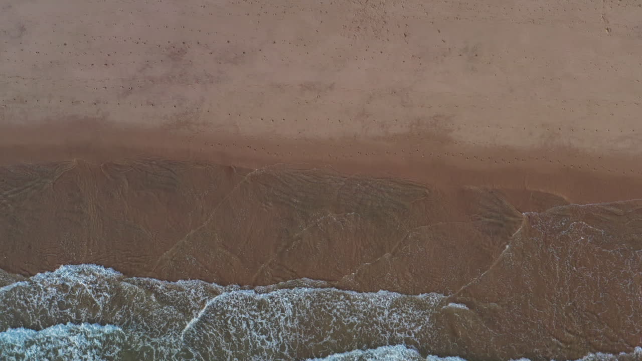 Aerial top view truck shot of ocean waves rolling on white sandy beach