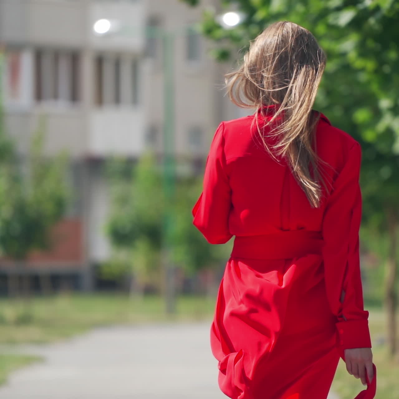 Slow motion of woman walking outdoors. Back view of a young female in red dress in the city. Long hair of attractive girl.
