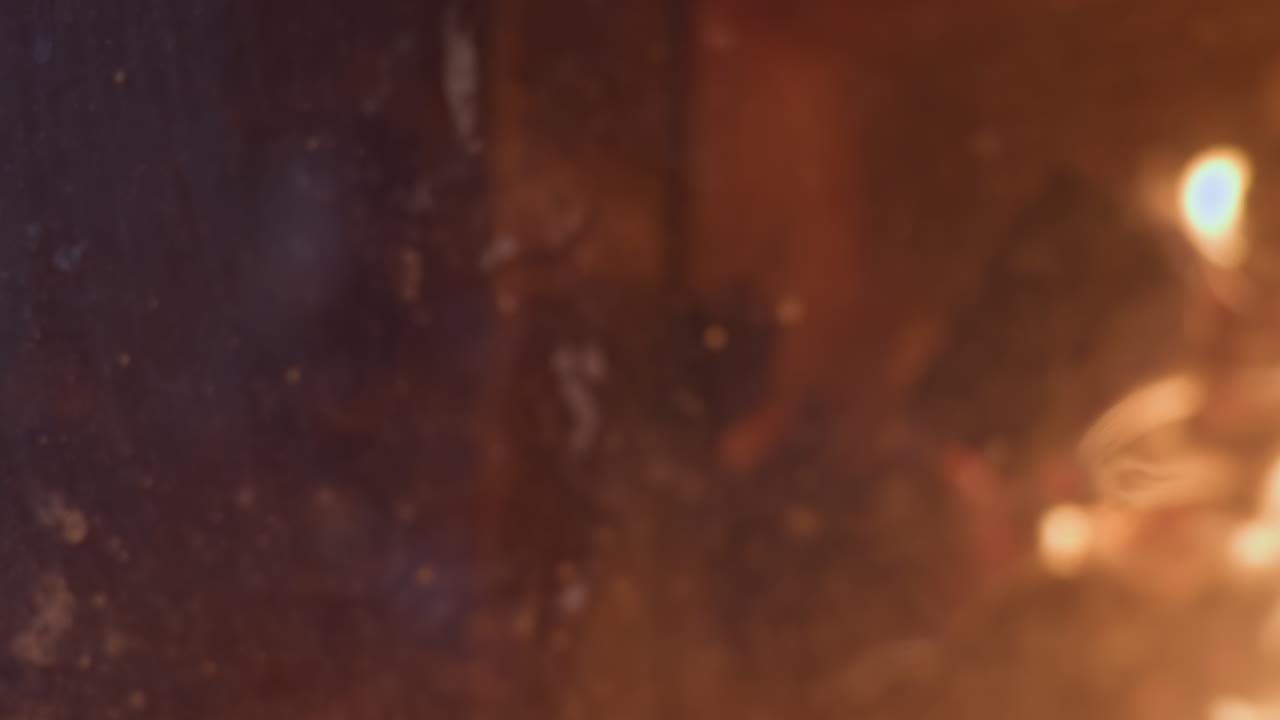 Soft blurred reflection of woman seated near fireplace captured on warm chimney glass, with glowing firewood and flames visible in background