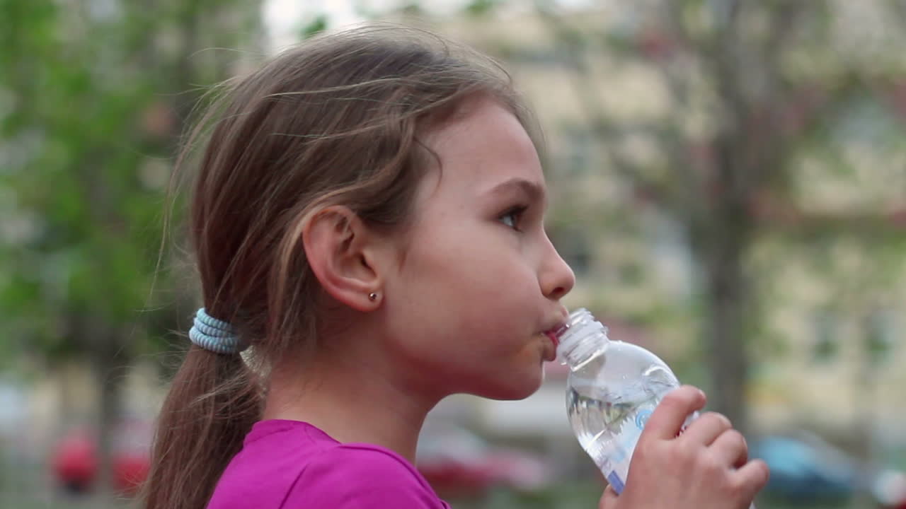 niño bebiendo agua de la botella al aire libre. niña con botella de agua en la mano