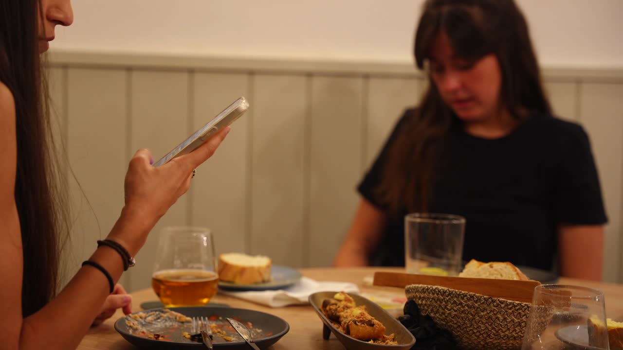 Two people sit at a cafe table, using their smartphones, with drinks and food in front of them