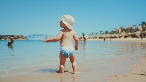 Sweet-baby-boy-walking-in-warm-seawater-at-coastline-in-summer-holiday.