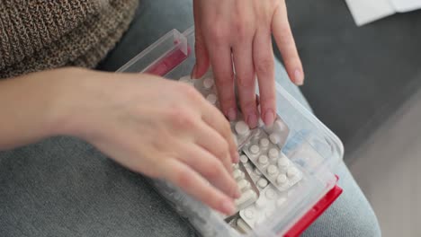 hands sorting various medications and pills in blister packs within a clear plastic container