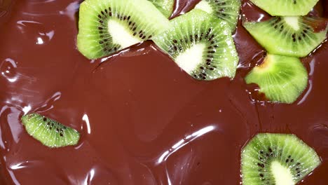 kiwi slices being covered in melted chocolate