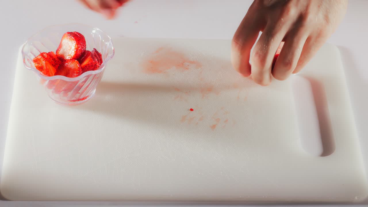 alcance las manos sobre una tabla de corte blanca, coloque las fresas en rodajas en una taza sobre un fondo blanco limpio