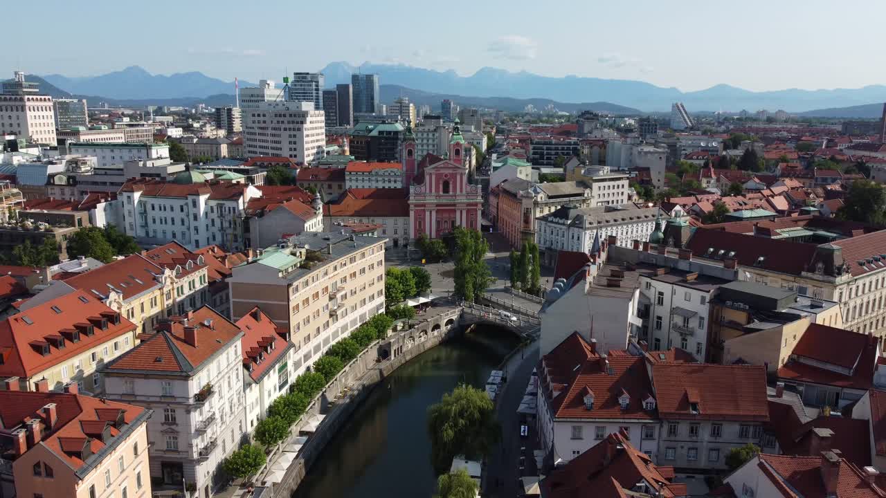 Aerial drone view of the wonderful city of Ljubljana on a summer's morning with city and mountains in background, Tromostovje bridge and Ljubljanica river