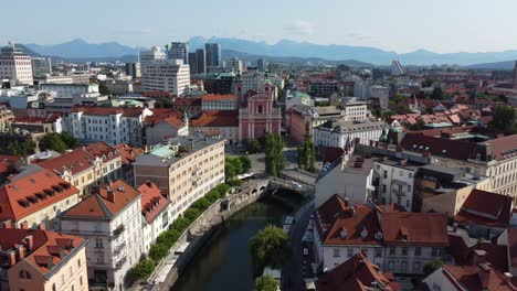 aerial drone view of the wonderful city of ljubljana on a summer's morning with city and mountains in background, tromostovje bridge and ljubljanica river