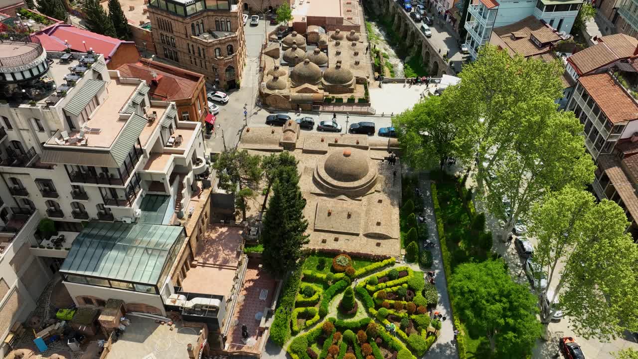Drone view the greenery of Tbilisi Botanical Garden area and the nearby Abanotubani sulfur baths, surrounded by traditional buildings and tree-filled courtyards