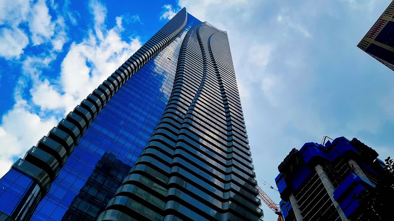 Yonge and Bloor looking up mirrored clouds on modern buildings sunny day while new skyscrapers are being built and birds are flying over and the weather is changing
