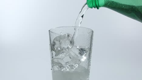 Pouring-mineral-sparkling-water-from-a-green-bottle-in-slow-motion,-static-shot-into-a-glass-with-ice