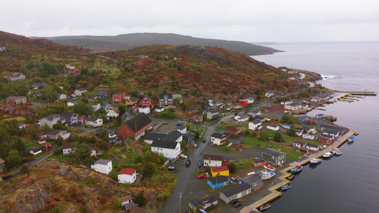 A stunning aerial shot of Petty Harbour Newfoundland in autumn featuring colorful houses winding roads and tranquil harbour waters set against rolling hills under crisp fall skies