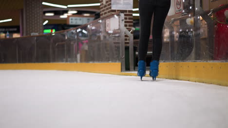 close-up of someone skating in blue skates with black trousers on an ice rink, with other people skating