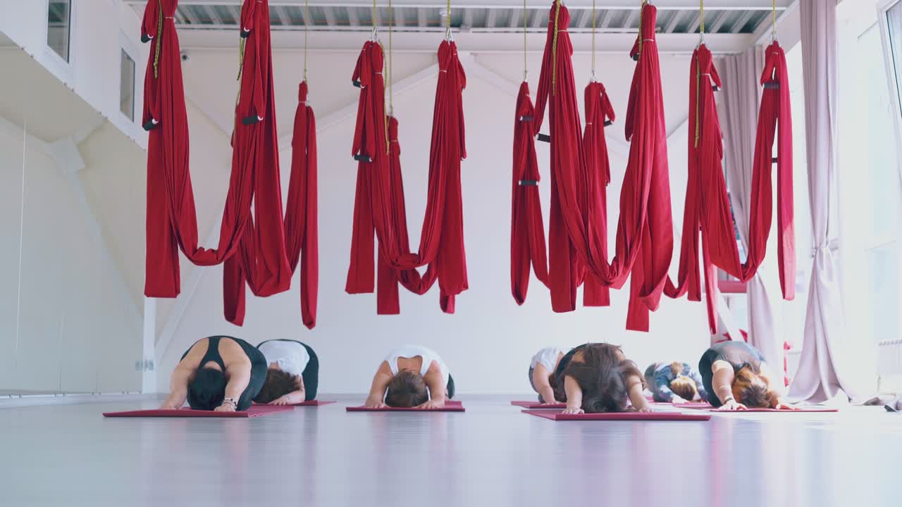 damen sitzen in einer ausgedehnten kinderpose unter fliegen-yoga-hängematten
