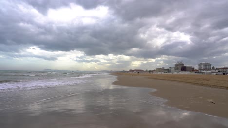 Sandy beach in the tourist area of   Italy, Rimini. It's cloudy with few people. You can see the hotel chains and the sea on the beach