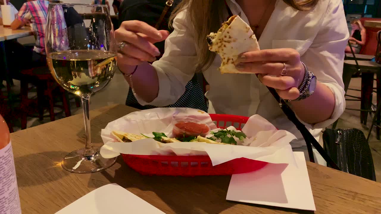 joven atractiva con un reloj en la mano prueba la comida oriental en la mesa donde se encuentra una copa de vino, cámara lenta en 4k