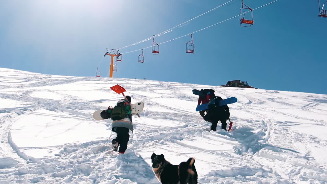 Slow motion: Snow boarders walking up the mountain. Camera moving slowly behind group of snowboarder walking up the mountain