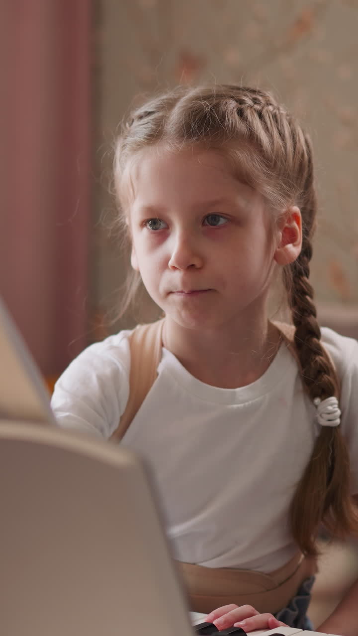 Demure schoolgirl in orthopedic corset stands by synthesizer flipping pages with notes. Clever child practices playing piano at home. Musical giftedness