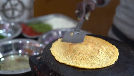Close-up-shot-of-making-Indian-breakfast,-a-man-making-Dosa-or-chilla-and-tapping-on-it-to-fry-well-on-the-stove