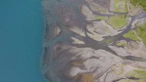 Aerial-top-down-shot-showing-river-delta-on-Iceland-Island-flowing-into-blue-ocean---scenery-pattern-from-above