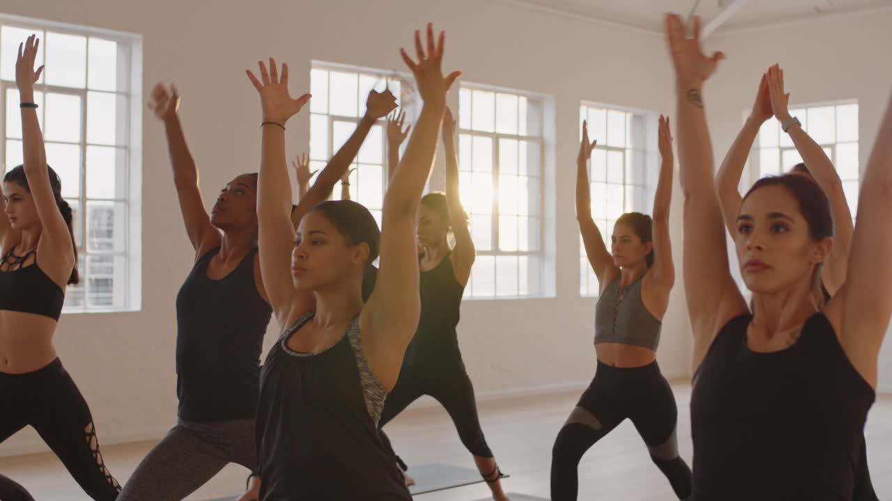 전사 포즈를 연습하는 다인종 여성들의 요가 수업 그룹은 일출 때 피트니스 스튜디오에서 건강한 생활 방식을 즐기고 있습니다.