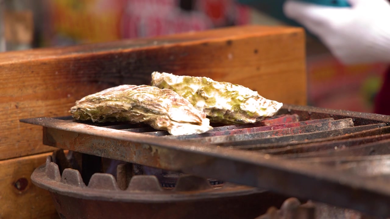 Close-up shot of fresh oysters cooking on a metal grill over an open gas flame