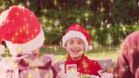 Animation-Von-Weihnachtlich-Leuchtenden-Sternen-über-Einer-Kaukasischen-Familie-Mit-Weihnachtsmützen-Am-Weihnachtstisch