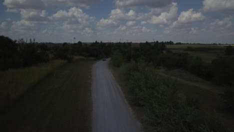 Aerial-tracking-shot-of-a-red-car-traveling-down-a-quiet-road