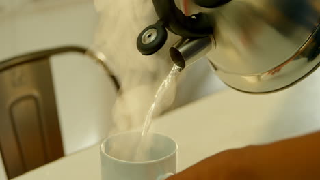 Close-up-of-black-woman-pouring-hot-water-in-coffee-cup-at-dinning-table-in-kitchen-4k