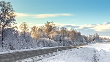 time lapse shot of flying clouds at blue sky during snowy winter day - melting ice frost on rural road beside snowy fields