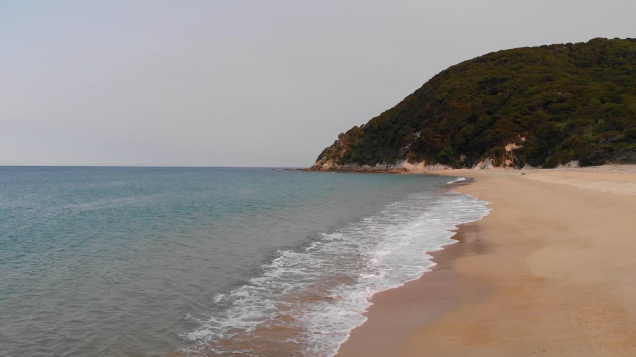 низкий полет над спокойным морем с ласковыми волнами поздним летним днем на отдаленном побережье новой зеландии в 4k, романтический безлюдный пляж