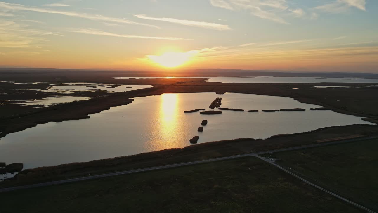 Flying with drone over serene wetland with calm waters and sunset.