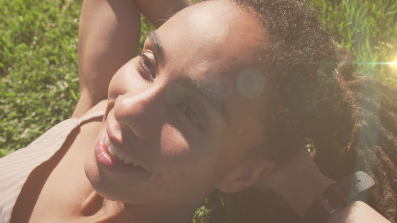 animación de puntos de luz sobre una mujer biracial sonriente tendida en el parque
