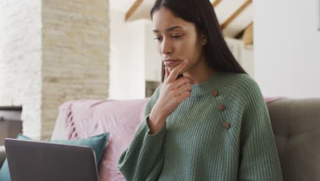 biracial woman using laptop and working in living room